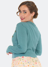 Load image into Gallery viewer, A woman wearing a teal blue long-sleeve knit cardigan with gold button details on the back, paired with a floral skirt, photographed against a light gray background.