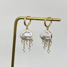 Load image into Gallery viewer, Pearl earrings with gold hooks and dangling crystals on a stand against a light gray background