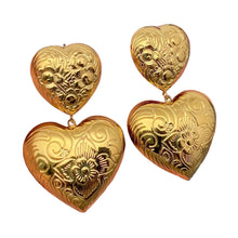 Load image into Gallery viewer, Gold heart-shaped earrings held in a hand against a gray background