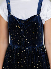 Load image into Gallery viewer, A close-up of a person wearing a navy velvet pinafore dress with a gold crescent moon and star pattern, layered over a white t-shirt.