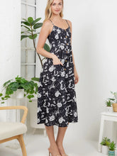 Load image into Gallery viewer, A woman modeling a black midi dress with a white cartoon cat print, featuring spaghetti straps, button details down the front, and side pockets, set against a bright white room with indoor plants.