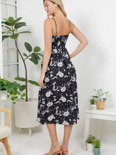 Load image into Gallery viewer, A woman modeling a black midi dress with a white cat print pattern, shown from the back in a bright, modern room with indoor plants.