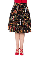 Load image into Gallery viewer, A black pleated A-line skirt with a colorful retro western-themed print featuring cacti, cowboy boots, and figures, shown on a model wearing red shoes and a red top against a white background.