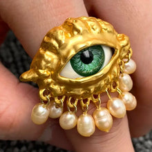Load image into Gallery viewer, Gold ring with an eye design and pearl accents held in a hand.
