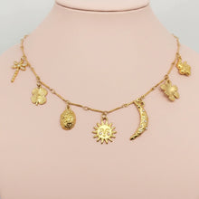 Load image into Gallery viewer, A gold charm necklace displayed on a pink mannequin bust. The necklace features multiple small charms including a dragonfly, clovers, a sun, a crescent moon, and a small bird.
