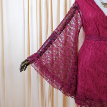 Load image into Gallery viewer, A close-up of a magenta lace dress or robe displayed on a mannequin, showing a wide sheer lace sleeve and a matching waist tie, set against a cream-colored curtain backdrop.