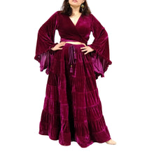 Load image into Gallery viewer, A woman wearing a deep magenta velvet two-piece outfit with a wrap-style long-sleeve top and tiered maxi skirt, standing against a white background with decorative autumn leaves.