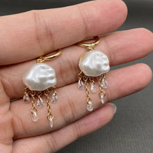 Load image into Gallery viewer, Pearl earrings with gold chains held in a hand against a neutral background
