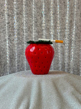 Load image into Gallery viewer, Red strawberry-shaped object with a cigarette on a textured surface
