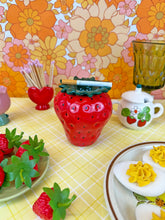 Load image into Gallery viewer, Strawberry-themed table setting with a red strawberry-shaped vase against a floral wallpaper background.
