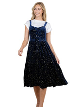 Load image into Gallery viewer, A woman models a dark navy blue velvet pinafore dress with gold celestial prints, layered over a white t-shirt. 
