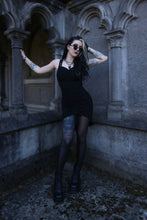 Load image into Gallery viewer, Woman in a black dress standing in an architectural setting with tattoos visible.
