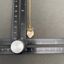 Load image into Gallery viewer, Necklace with a heart-shaped pendant on a gray surface with rulers for scale.
