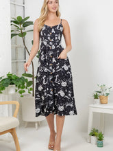 Load image into Gallery viewer, A woman modeling a black midi dress with a white cat pattern, standing in a bright room with indoor plants and furniture.
