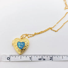 Load image into Gallery viewer, Heart-shaped gold locket with blue gemstone on a white background with a ruler for scale.
