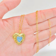 Gold heart-shaped locket with blue heart design on a hand