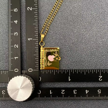 Load image into Gallery viewer, Gold necklace with a small book pendant on a ruler for scale
