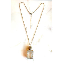 Load image into Gallery viewer, A gold-toned necklace with a rectangular clear glass or acrylic pendant, displayed on a light marble-like background.
