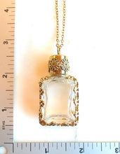 Load image into Gallery viewer, A vintage gold-toned glass perfume bottle pendant necklace with a matching chain, displayed on a white background with a ruler on the left and bottom edges for scale.
