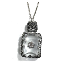 Load image into Gallery viewer, A silver-toned necklace featuring a rectangular clear glass bottle pendant with ornate filigree silver cap and border, accented by a small flower-shaped crystal detail on the front, shown against a plain white background.
