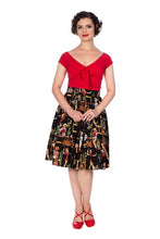 Load image into Gallery viewer, A woman modeling a retro-style two-piece dress with a bright red top and a black pleated skirt featuring a colorful vintage illustration print, paired with red shoes against a plain white background.
