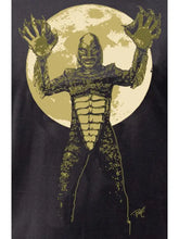 Load image into Gallery viewer, A close-up of a graphic print on a black garment, featuring a stylized creature with raised clawed hands standing in front of a large cream-colored moon.
