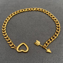 Load image into Gallery viewer, A gold-tone chain bracelet with a heart-shaped clasp and an arrow charm, displayed on a textured gray fabric background.
