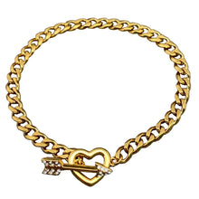 Load image into Gallery viewer, A gold-tone Cuban link chain bracelet with a heart-shaped charm pierced by a small arrow adorned with clear rhinestones, displayed on a textured gray background.
