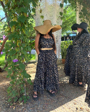 Load image into Gallery viewer, Two women in floral dresses and wide-brimmed hats standing outdoors near a tree.
