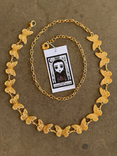 Load image into Gallery viewer, Gold butterfly necklace on a textured brown surface with a card attached.
