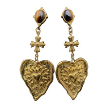 Load image into Gallery viewer, Gold heart-shaped earrings with cross details on a black stand.
