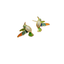Load image into Gallery viewer, A pair of gold-toned bird stud earrings with green, orange, and blue enamel details and clear pavé stones on the chest, shown resting on a person's fingers against a white background.
