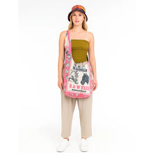 Load image into Gallery viewer, A woman stands against a white studio background wearing a pink printed crossbody bag with horse graphics, a green strapless top, beige pants, white sneakers, and a colorful bucket hat.
