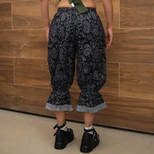 Load image into Gallery viewer, Person wearing black patterned pants with ruffled cuffs against a wooden wall.
