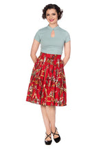 Load image into Gallery viewer, A woman modeling a light blue short-sleeve mock-neck top and a red pleated skirt with a vintage circus or carnival print featuring figures and balloons. She is wearing black patent mule heels against a solid white background.
