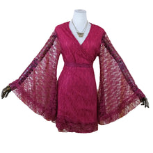 Load image into Gallery viewer, A magenta lace wrap dress with dramatic bell sleeves displayed on a mannequin against a cream-colored curtain backdrop.
