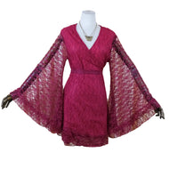 A magenta lace wrap dress with dramatic bell sleeves displayed on a mannequin against a cream-colored curtain backdrop.