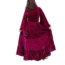 Load image into Gallery viewer, A woman wearing a long-sleeved, tiered magenta velvet maxi dress, photographed from behind against a white background with decorative autumn leaves.
